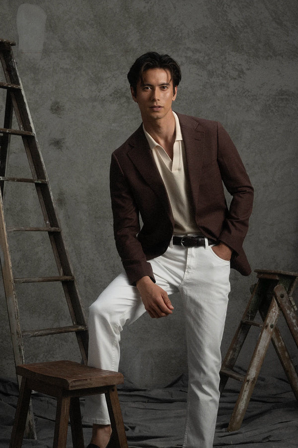 Man in a brown blazer and white pants standing in a studio setting with a ladder and stool.