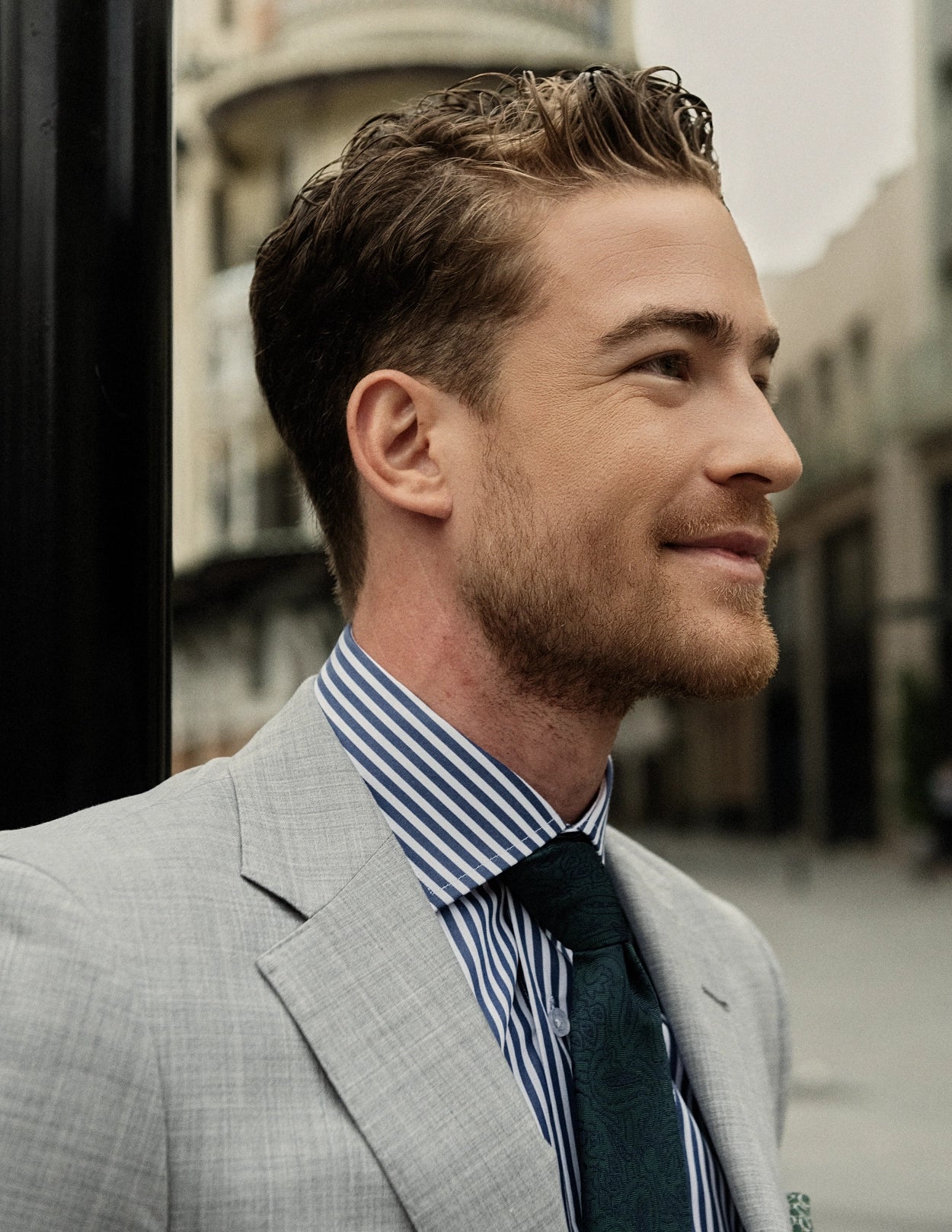 Man in a gray suit with a striped shirt and dark tie, standing outdoors.