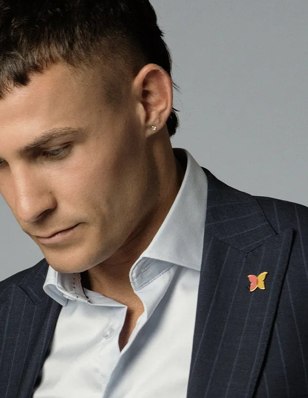 Man wearing a dark suit with a Beyond Blue pin on a grey background