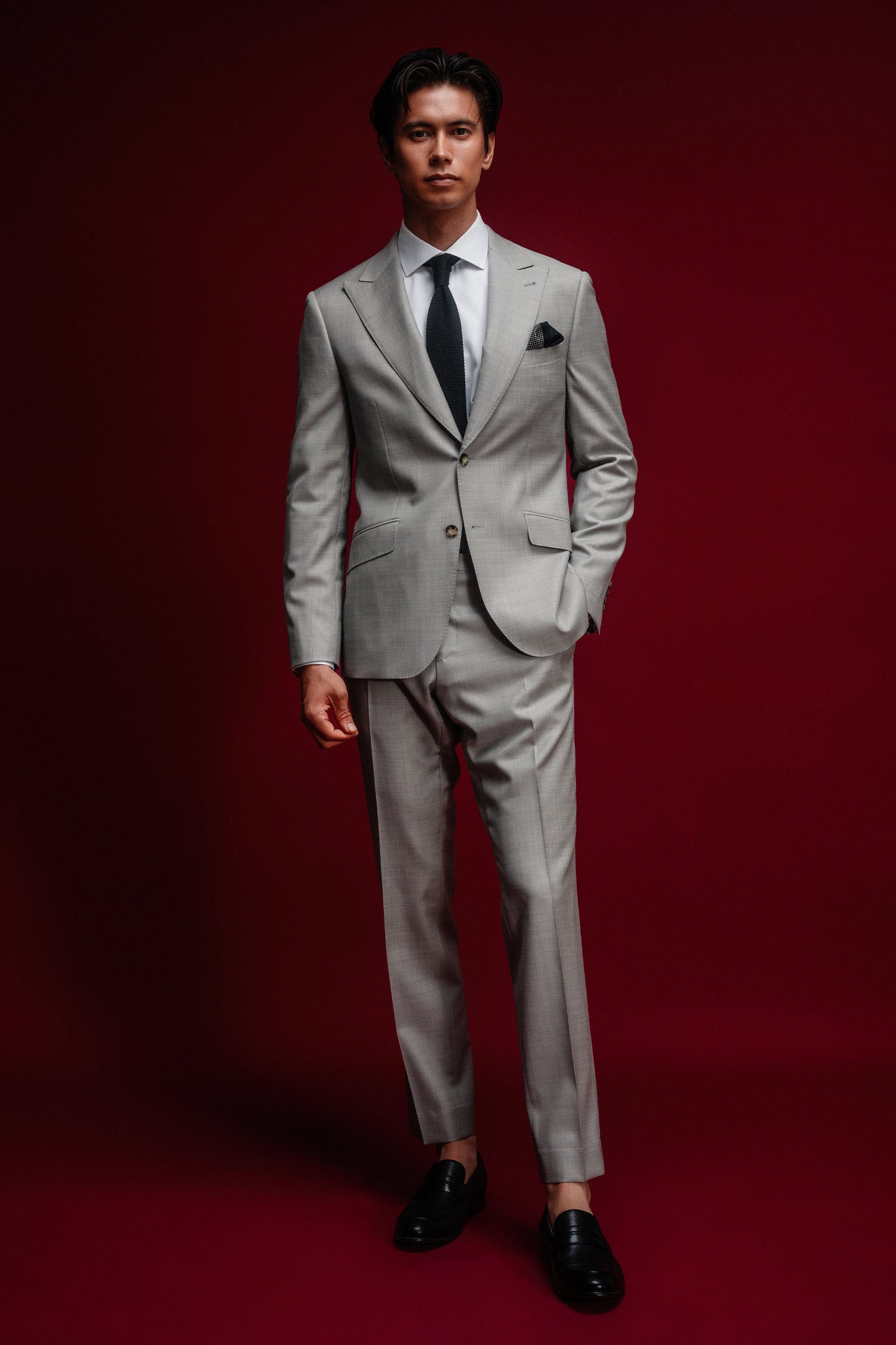 Man wearing a gray suit with a black tie against a red background