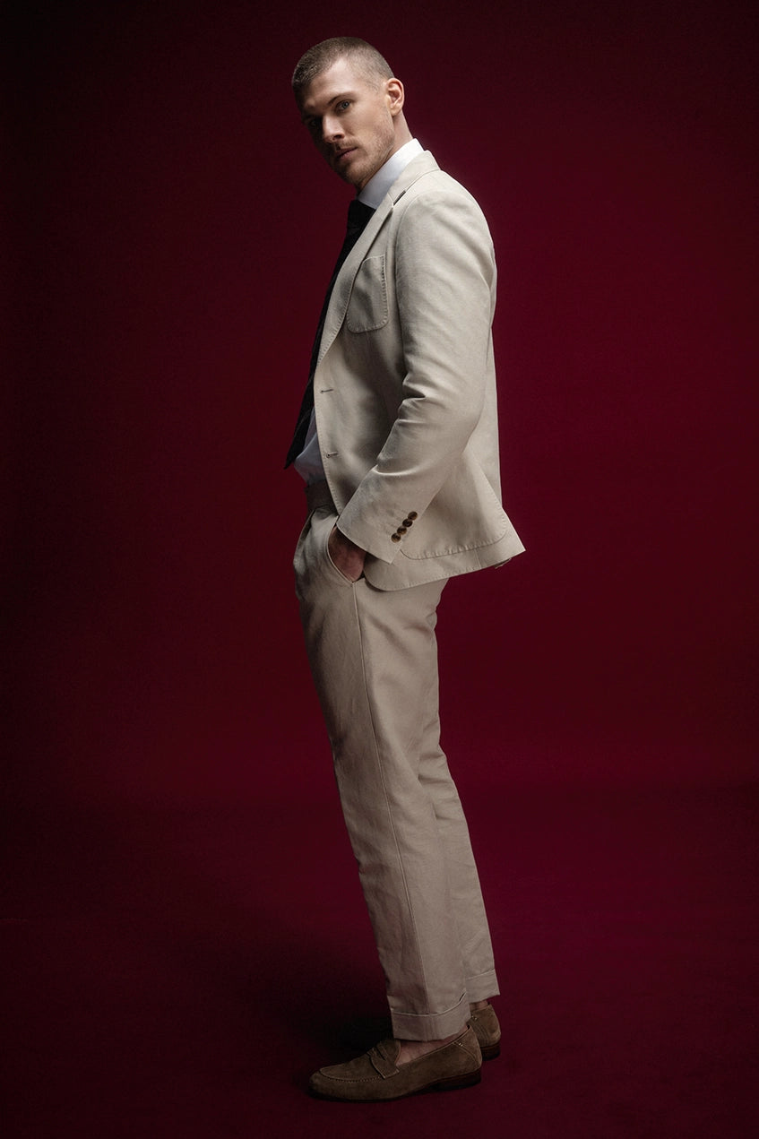 Man in a beige suit standing against a red background