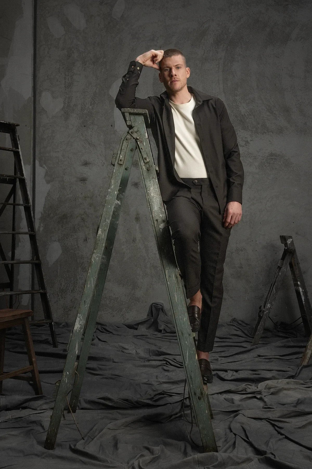 Man standing on a vintage ladder against a dark gray background