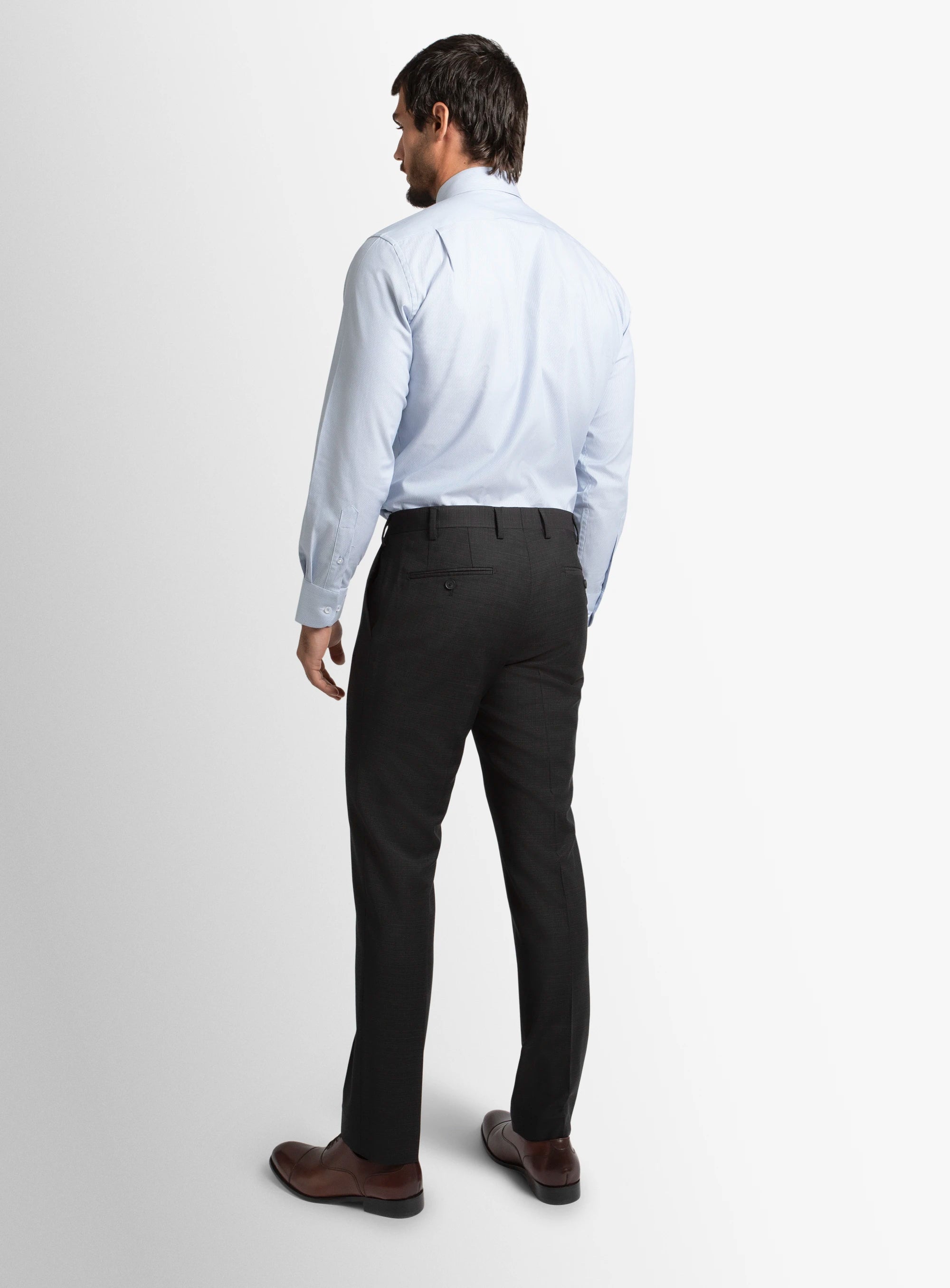 Man wearing a light blue dress shirt and black pants on a white background