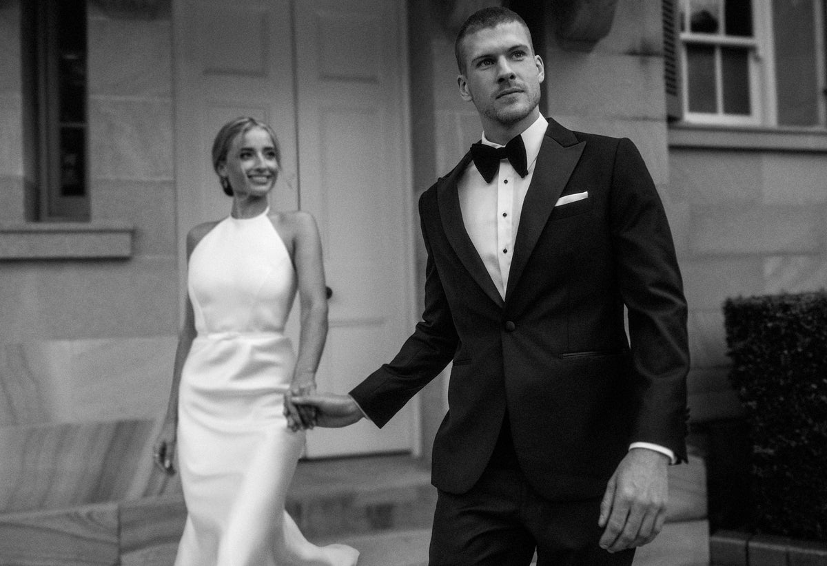 Man in a tuxedo and woman in a white dress standing outdoors.