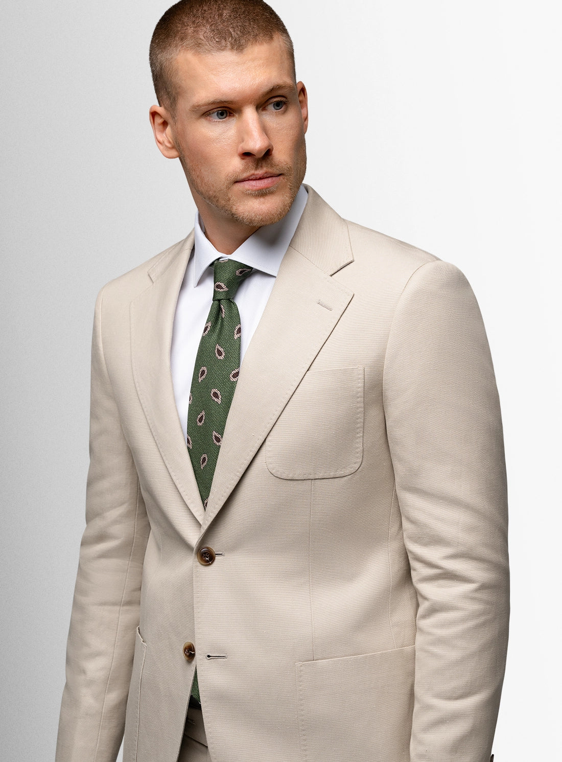 Man wearing a beige suit with a green patterned tie on a light gray background