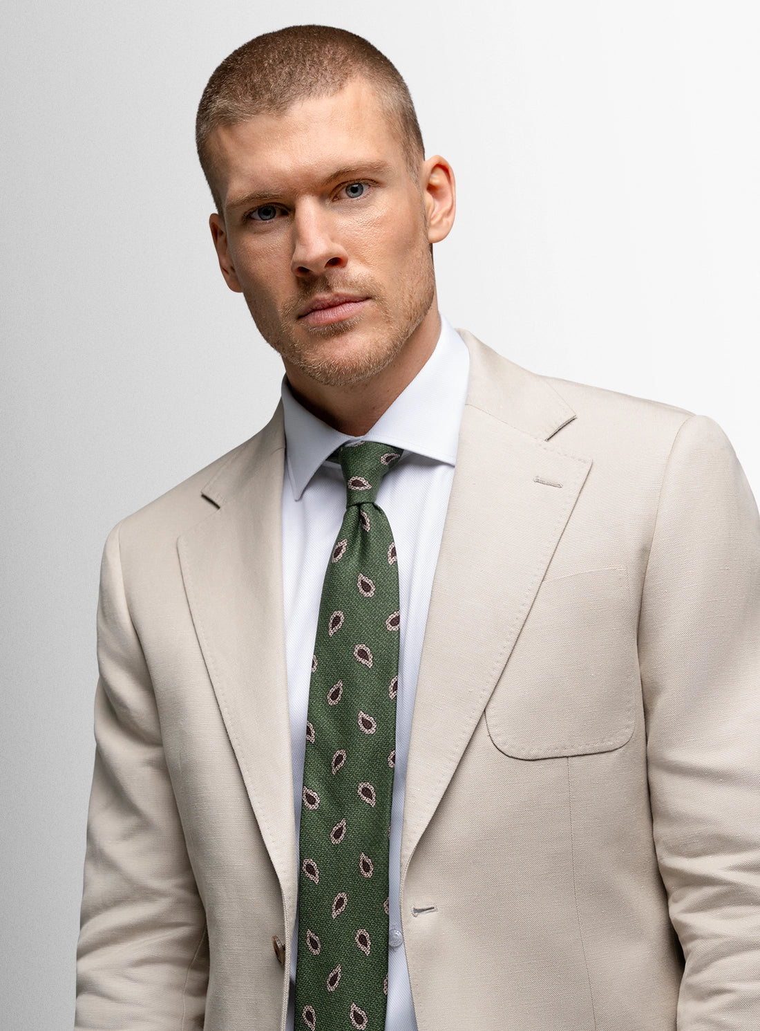 Man wearing a beige suit with a green patterned tie on a light gray background