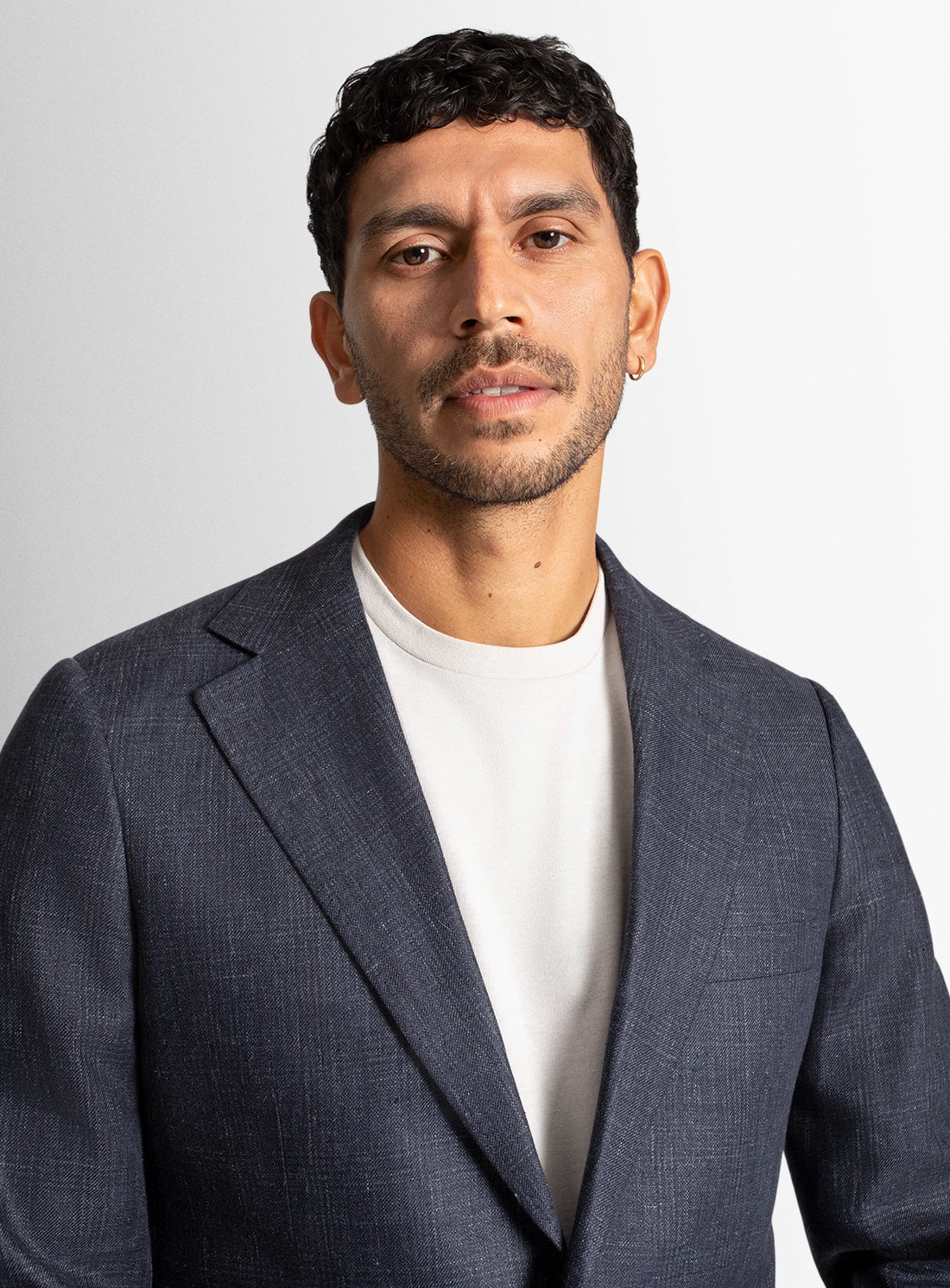 Man wearing a dark gray suit jacket over a white shirt on a plain background