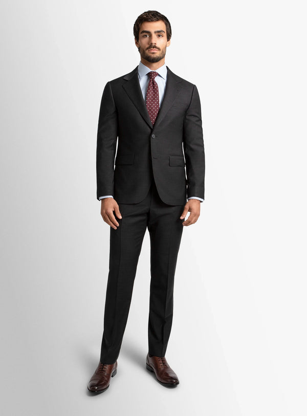 Man wearing a dark gray suit with a patterned tie on a light gray background