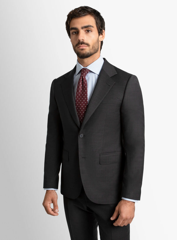 Man wearing a dark gray suit with a white shirt and patterned tie on a light gray background