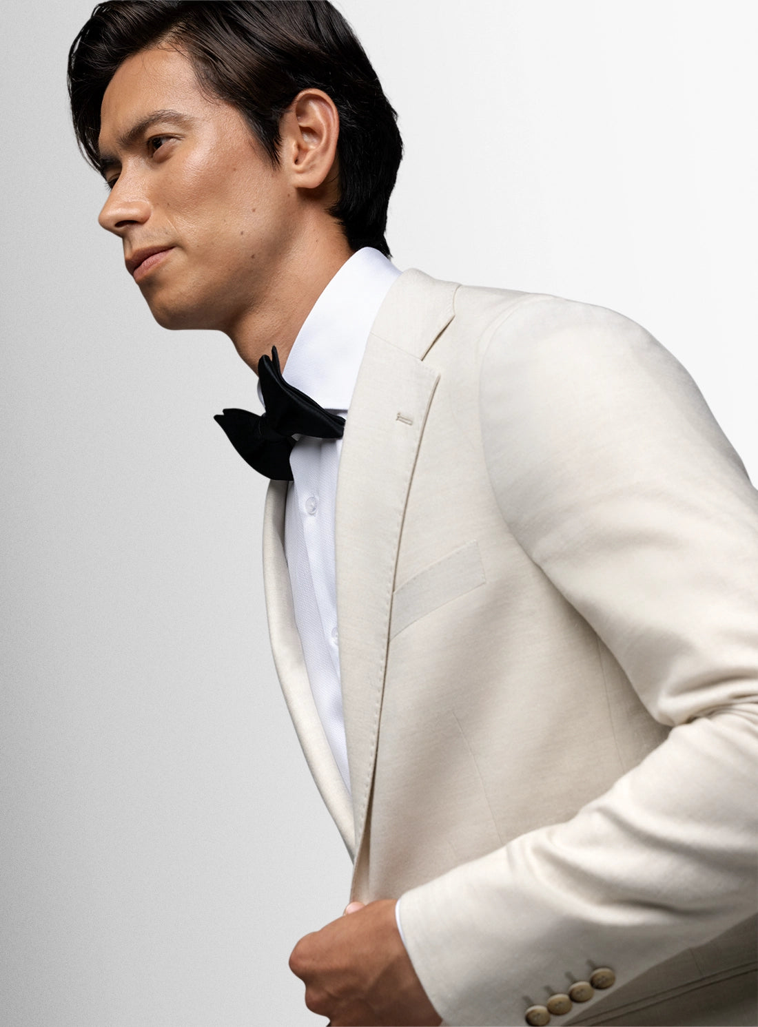 Man wearing a white suit with a black bow tie on a gray background