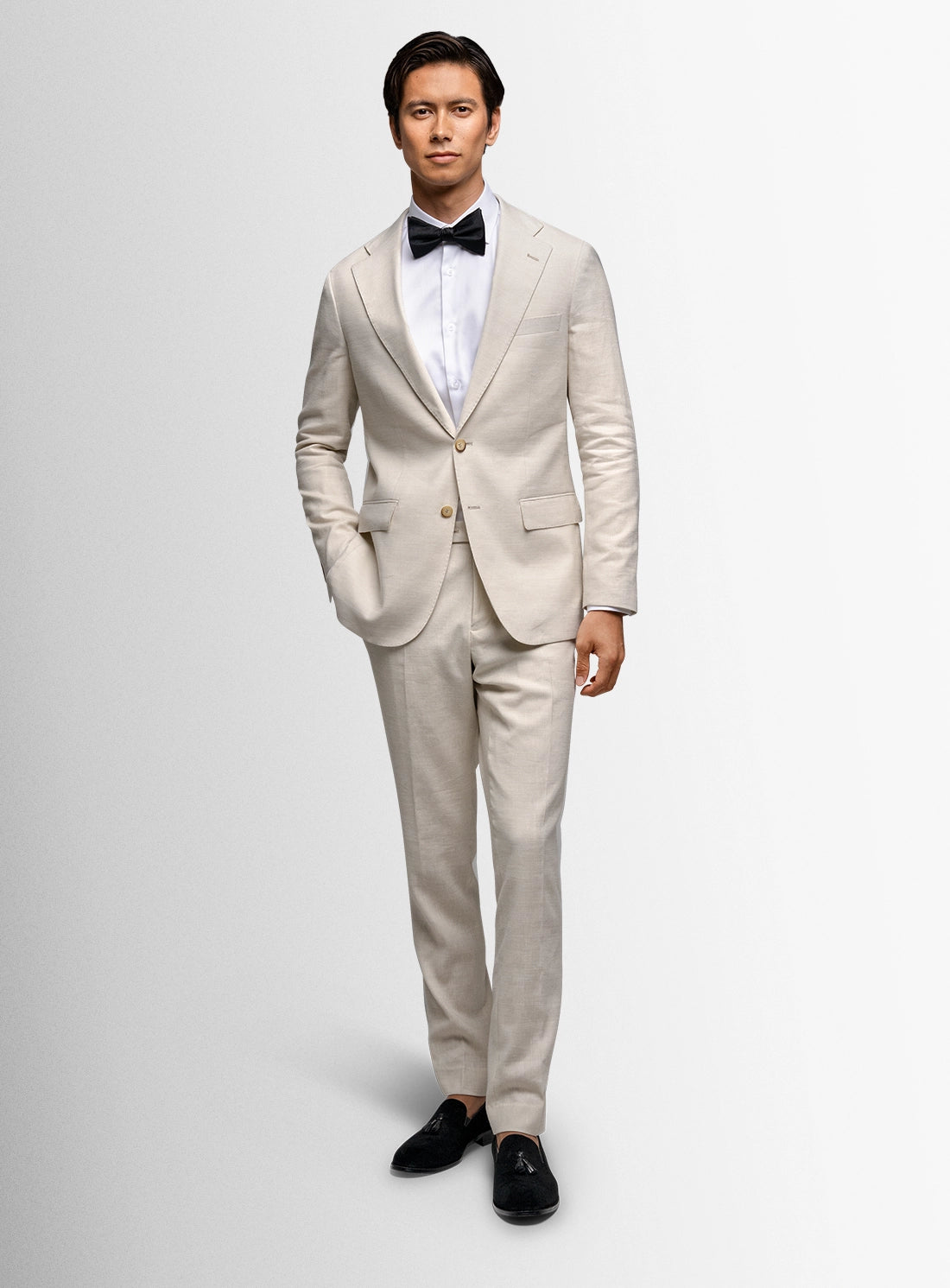 Man wearing a beige suit with a black bow tie on a white background