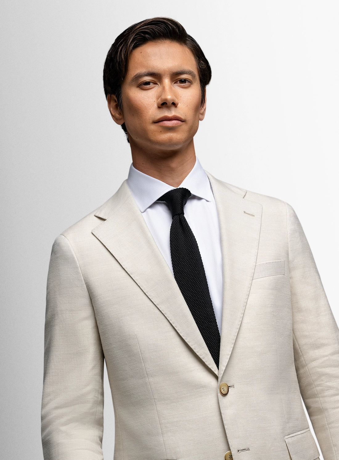 Man wearing a light beige suit with a white shirt and black tie on a plain background