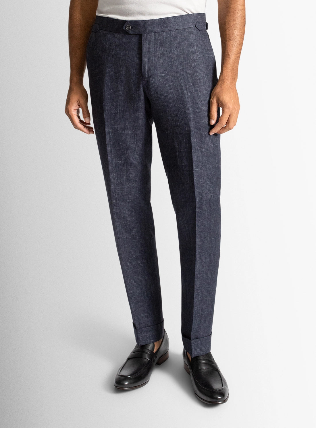Person wearing dark blue dress pants with a white shirt and black shoes on a light gray background