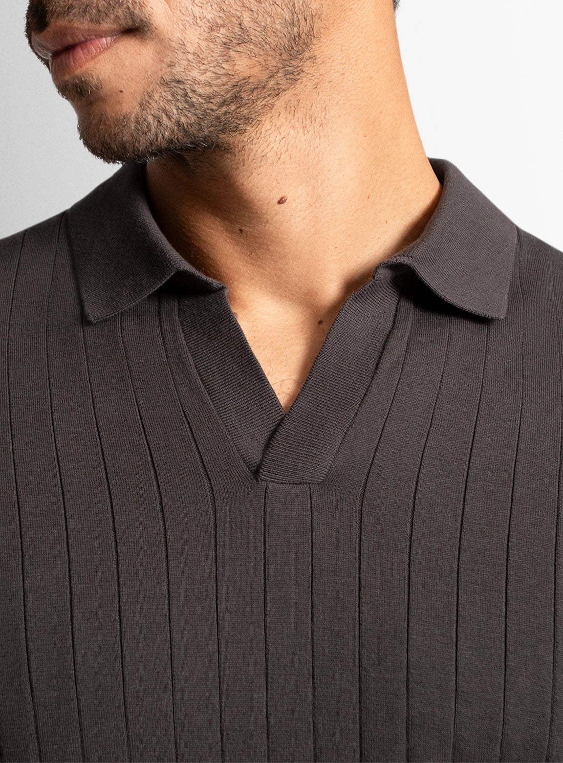 Close-up of a person wearing a dark brown ribbed sweater with a plain background