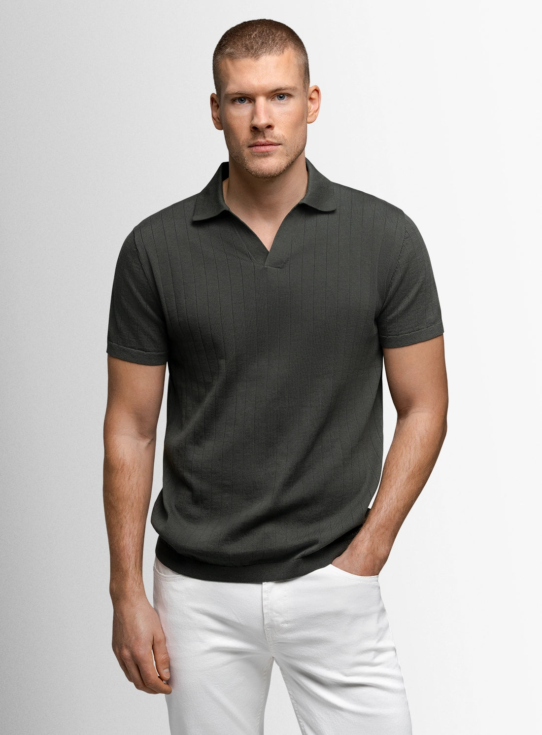 Man wearing a dark gray polo shirt and white pants on a light gray background