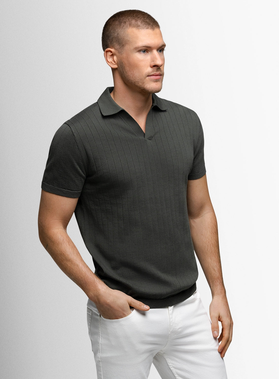 Man wearing a dark green polo shirt and white pants on a light gray background