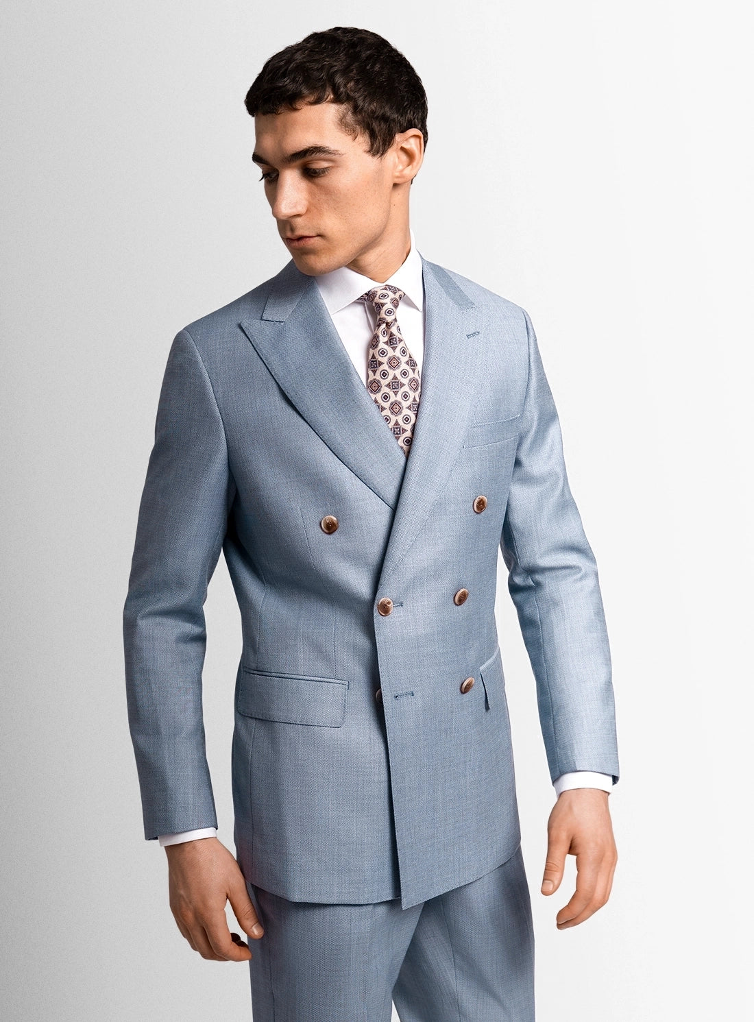 Man wearing a light blue suit with a patterned tie on a plain background