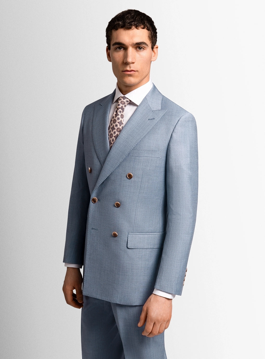 Man wearing a light blue suit with a patterned tie on a plain background