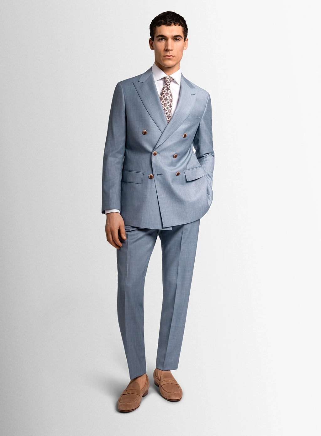 Man wearing a light blue suit with a white shirt and patterned tie on a plain background