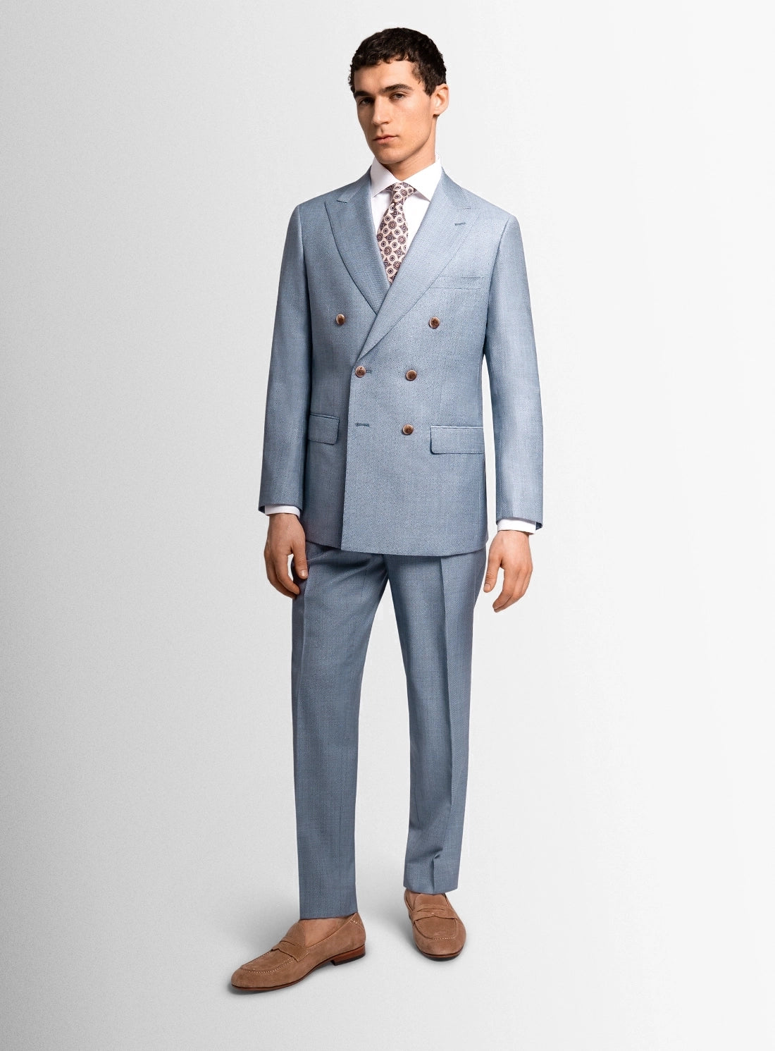 Man wearing a light blue suit with a white shirt and patterned tie on a plain background