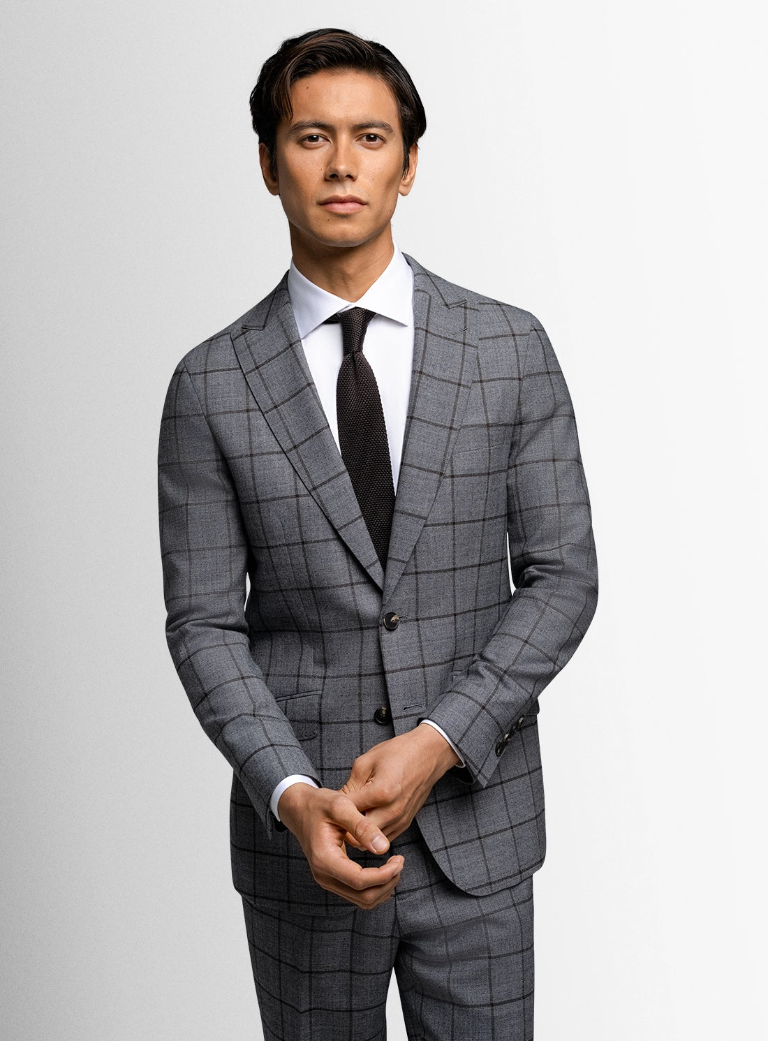 Man wearing a gray checkered suit with a white shirt and black tie on a light gray background