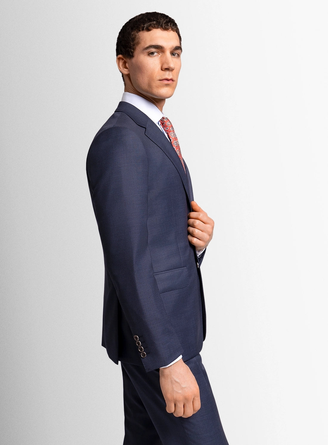 Man wearing a navy suit with a white shirt and patterned tie on a light gray background