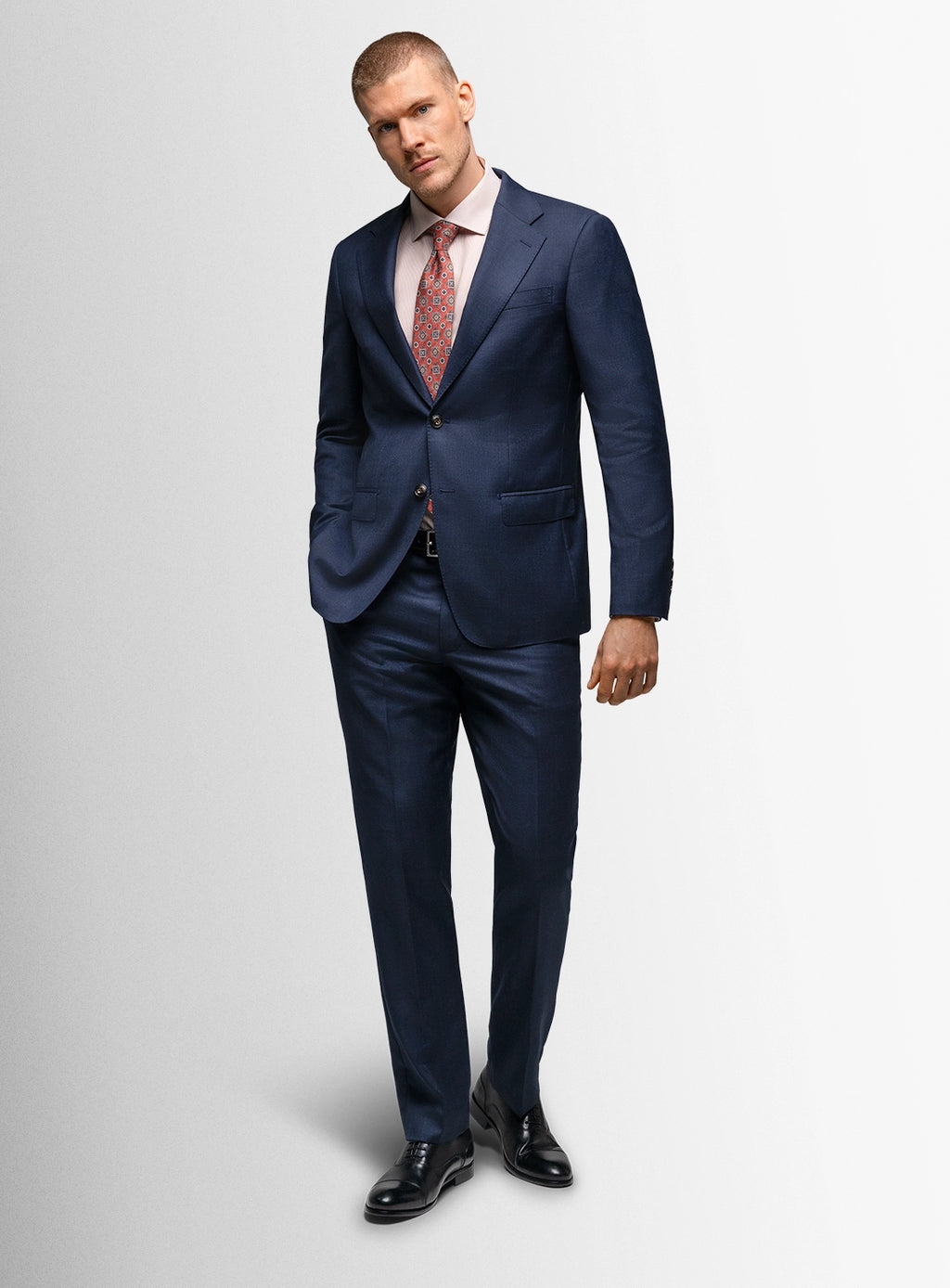 Man wearing a navy suit with a pink tie on a light gray background