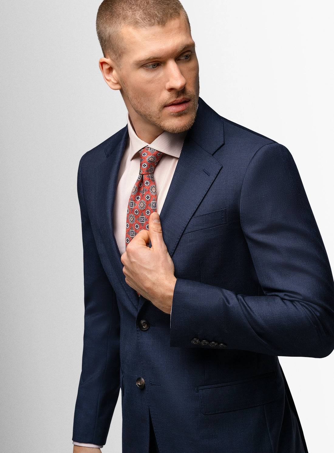 Man wearing a navy suit with a patterned tie on a light gray background