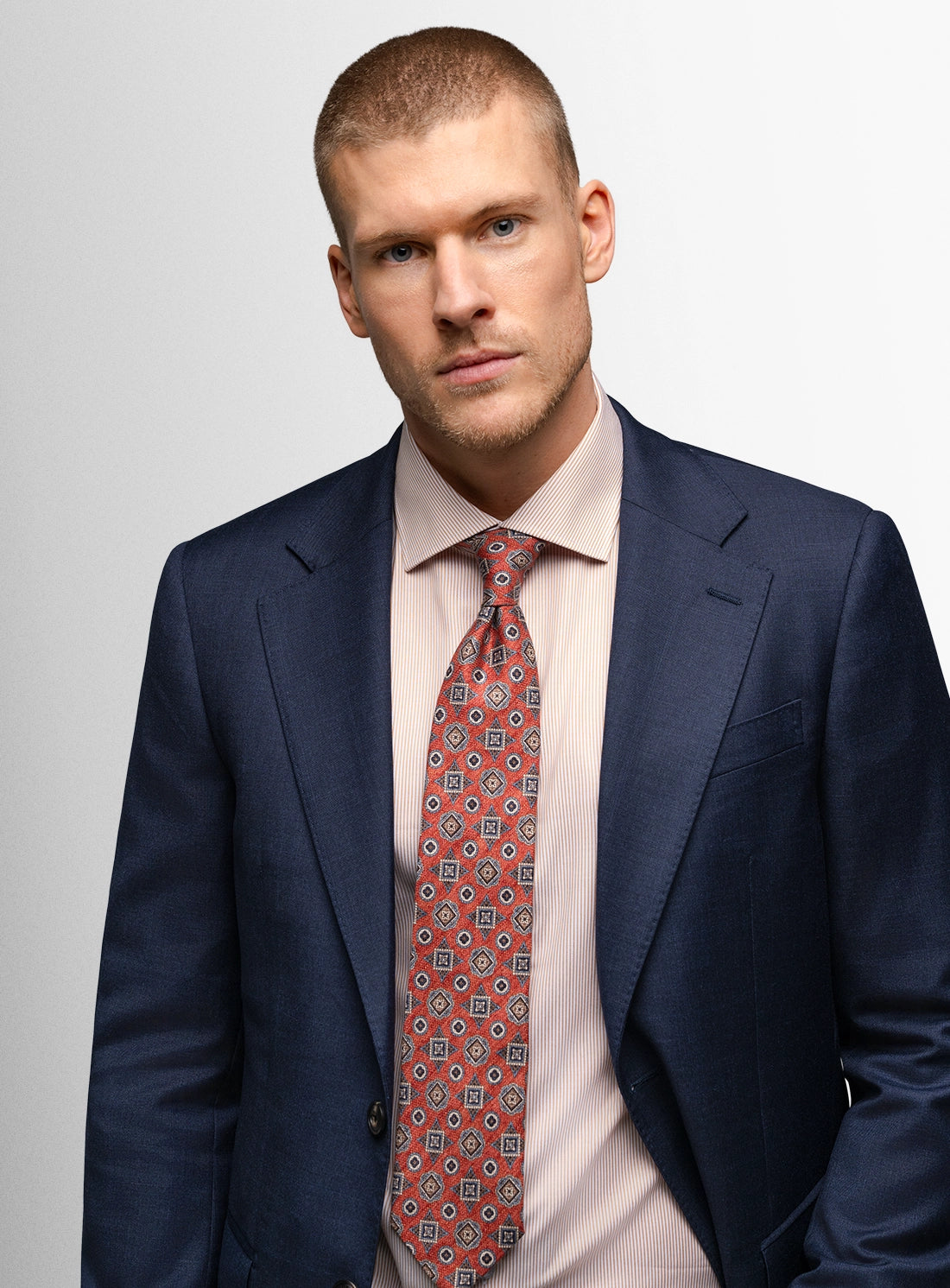 Man wearing a navy suit with a red patterned tie on a light gray background