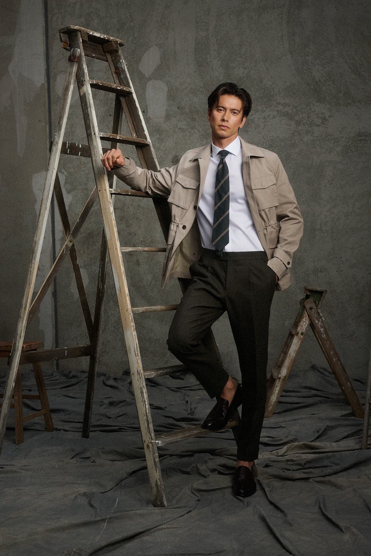 Man in a suit standing next to a ladder against a gray background