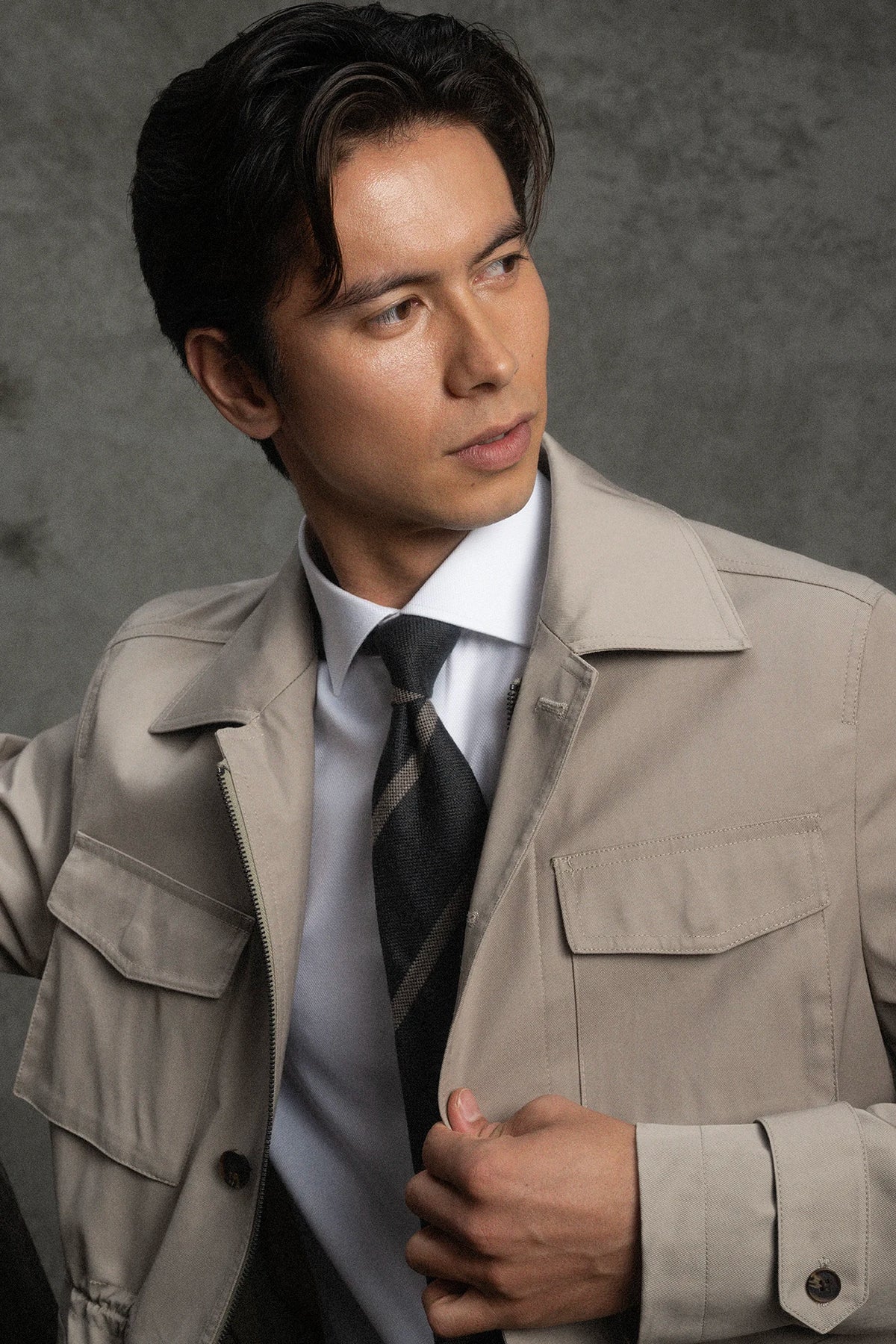 Man wearing a beige trench coat over a suit with a gray background