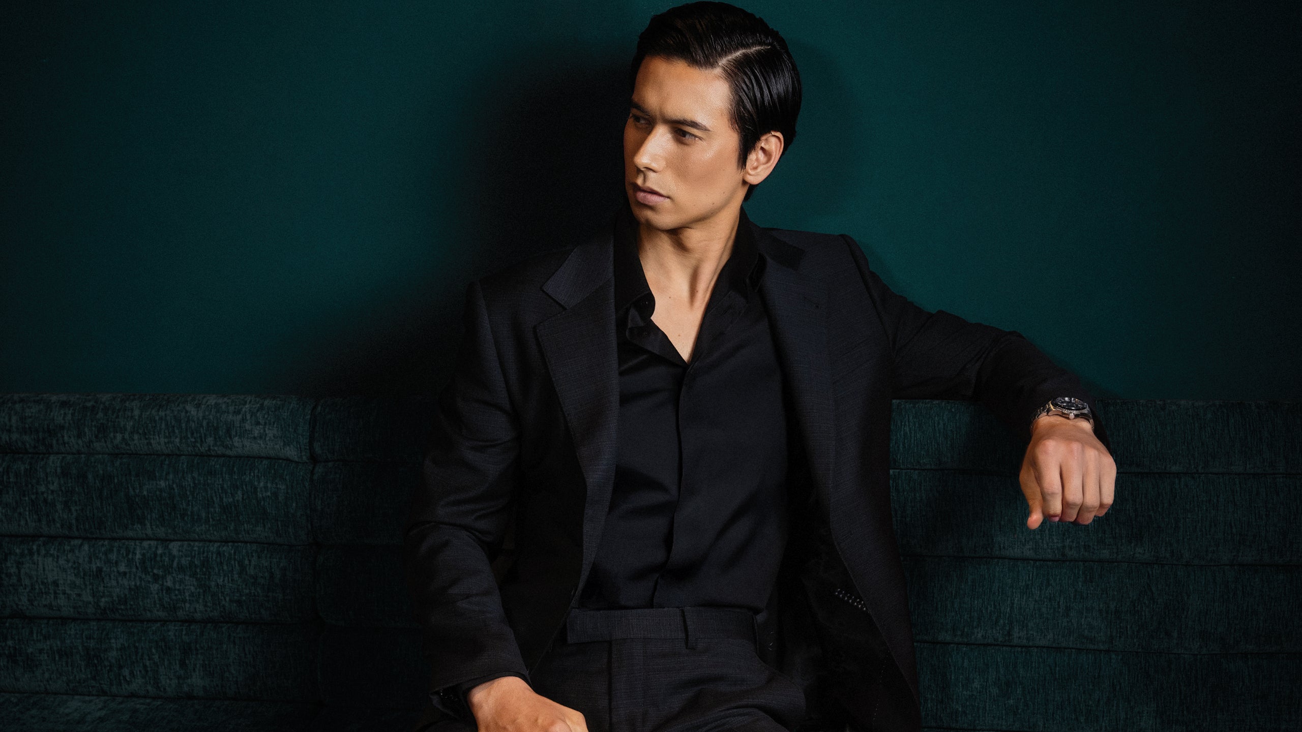 Man in a black suit sitting against a dark background