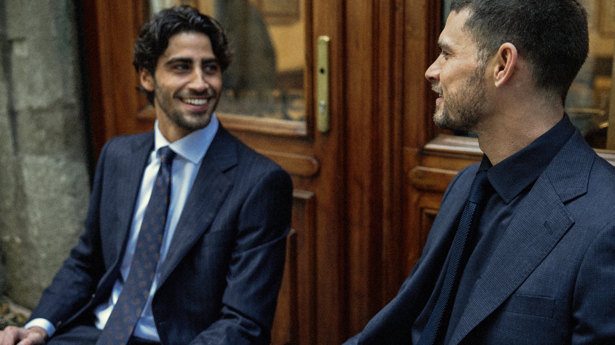 Two men in suits sitting next to each other in a formal setting.
