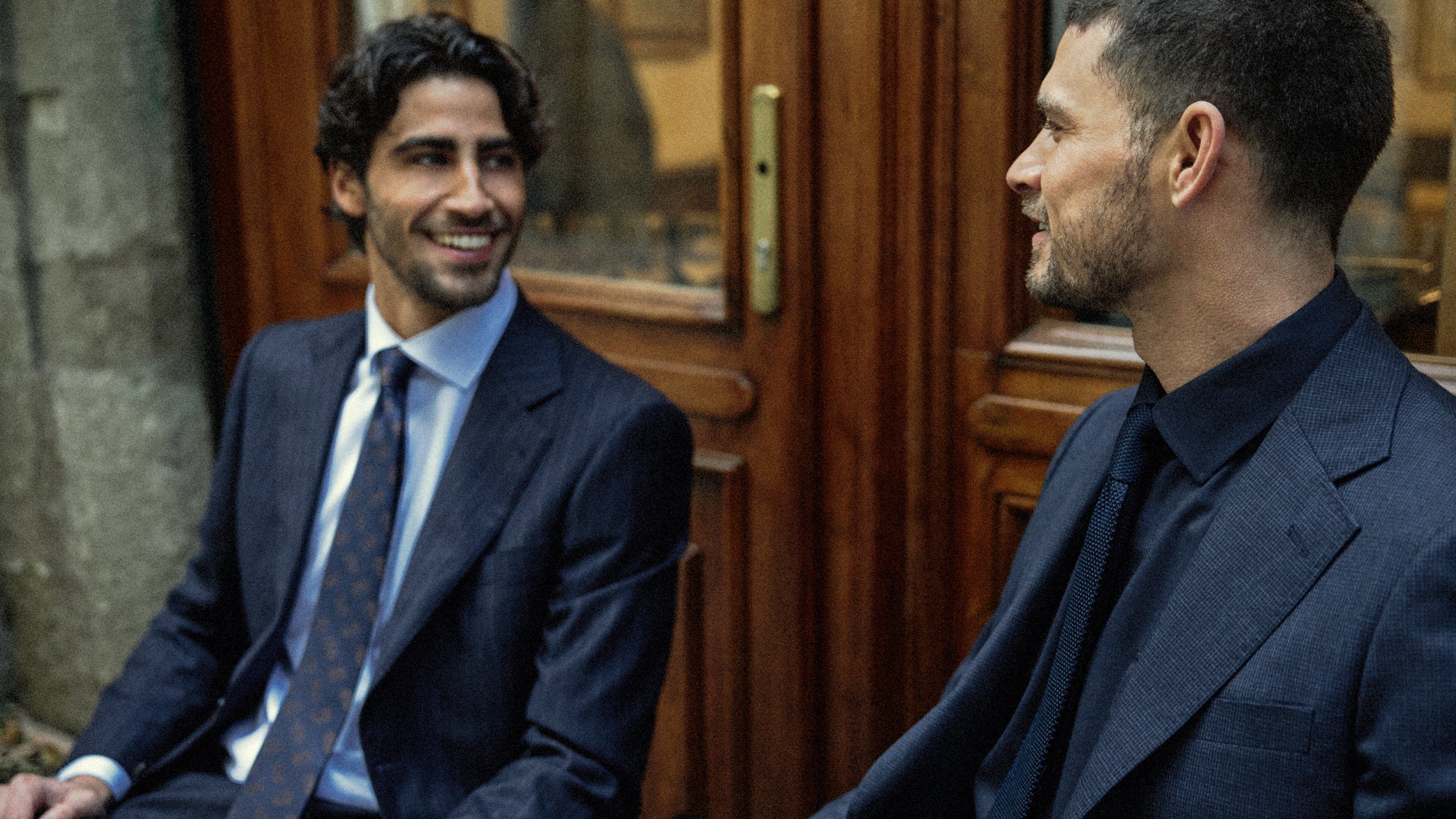 Two men in suits sitting next to each other in a formal setting.