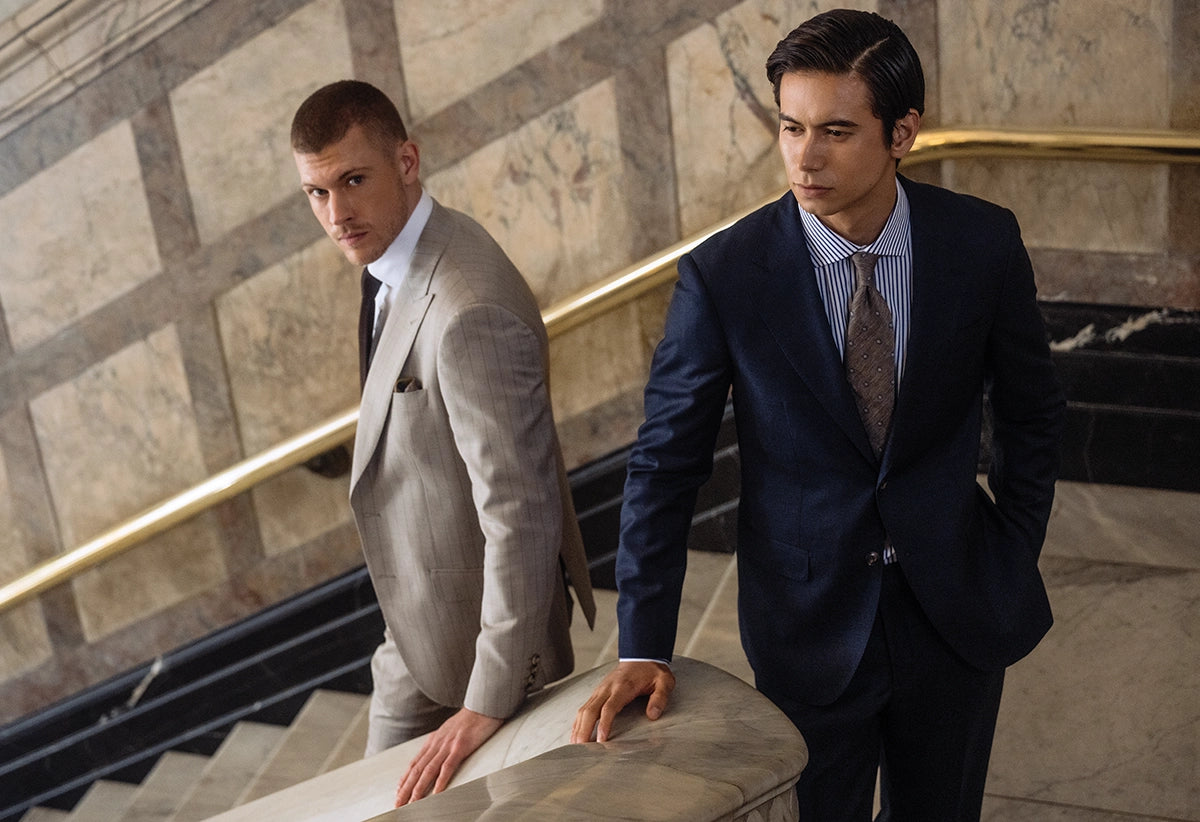 Two men in suits standing on a staircase with marble walls.