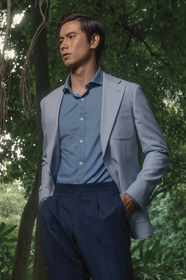Man in a light gray blazer and blue shirt standing in a forest setting