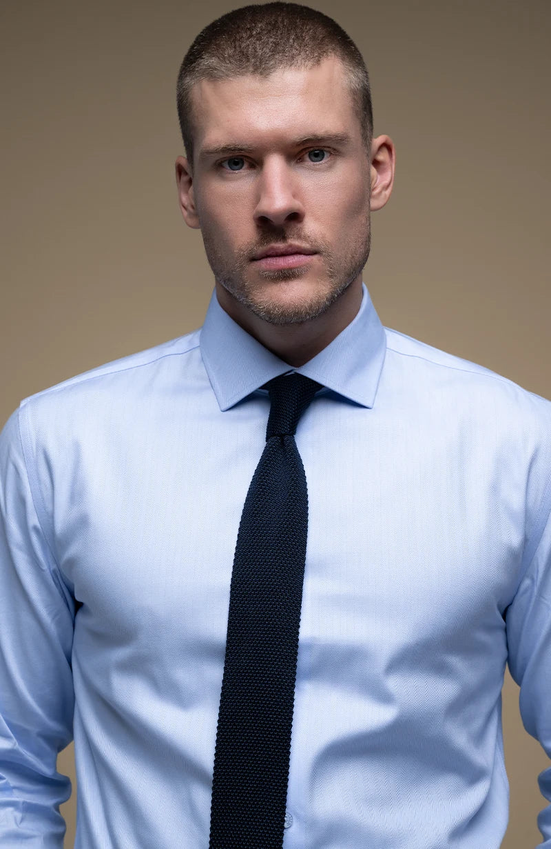 Man wearing a light blue shirt with a black tie against a beige background