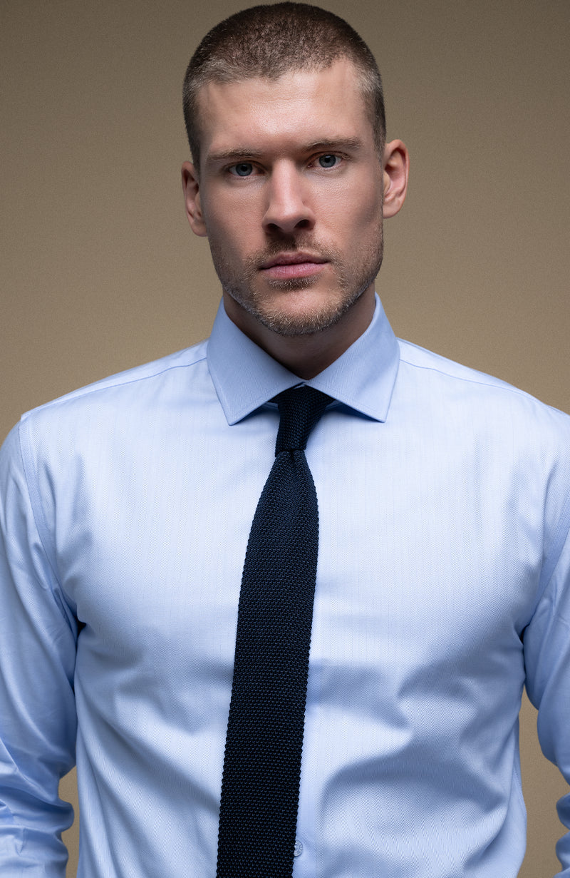 Man wearing a light blue shirt and black tie against a beige background