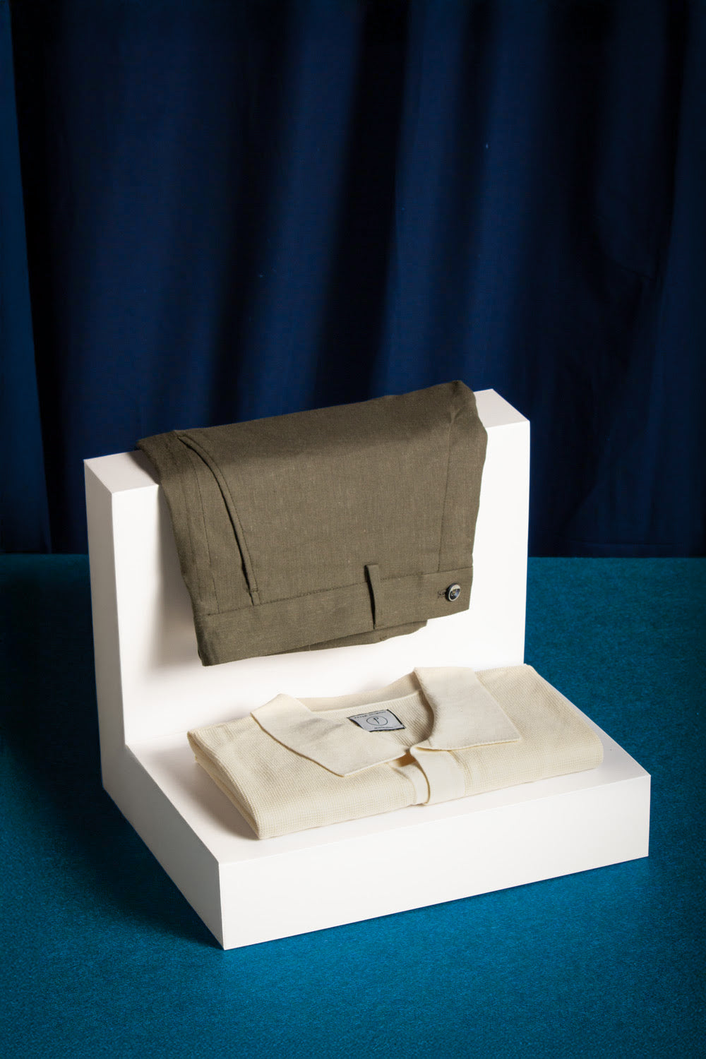 Green bag and beige shirt on a white stand against a dark blue background