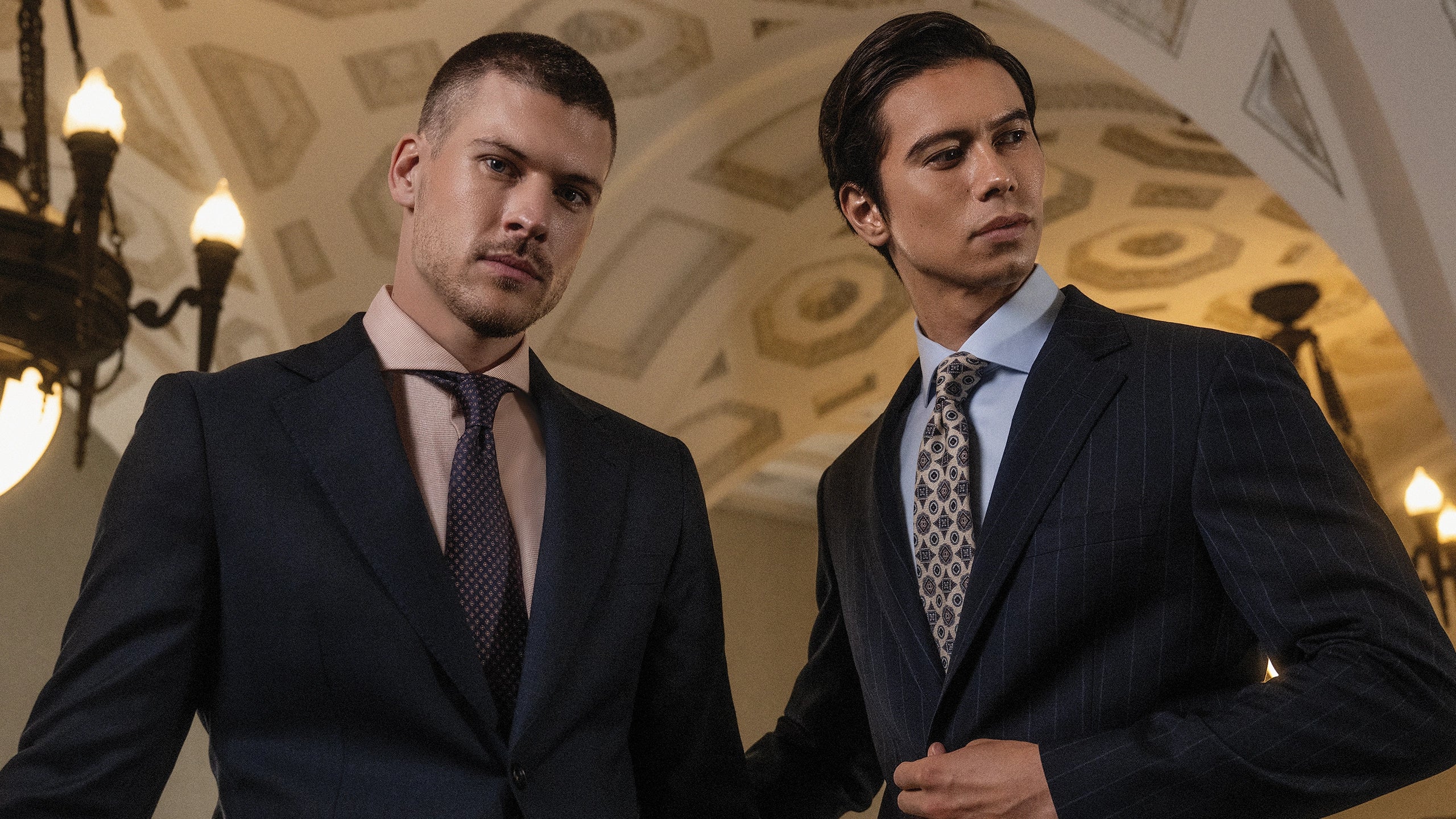 Two men in suits standing in a room with ornate ceiling