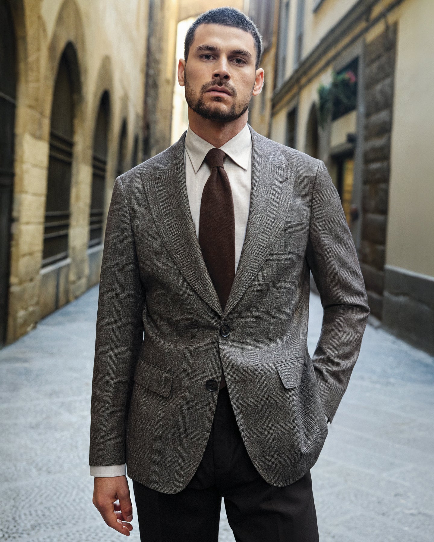Man in a gray suit with a brown tie standing in an urban alleyway.