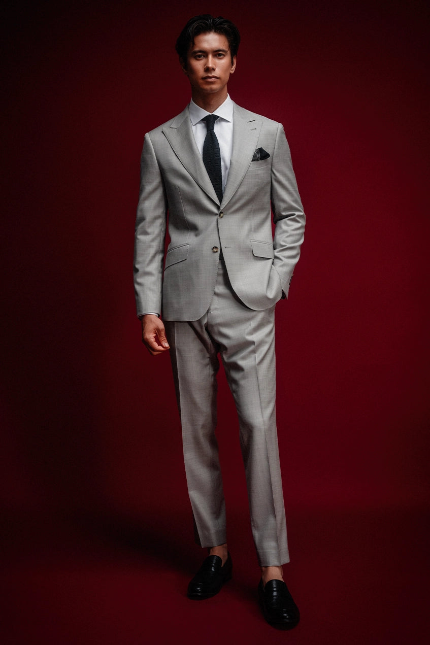 Man wearing a gray suit with a black tie against a red background