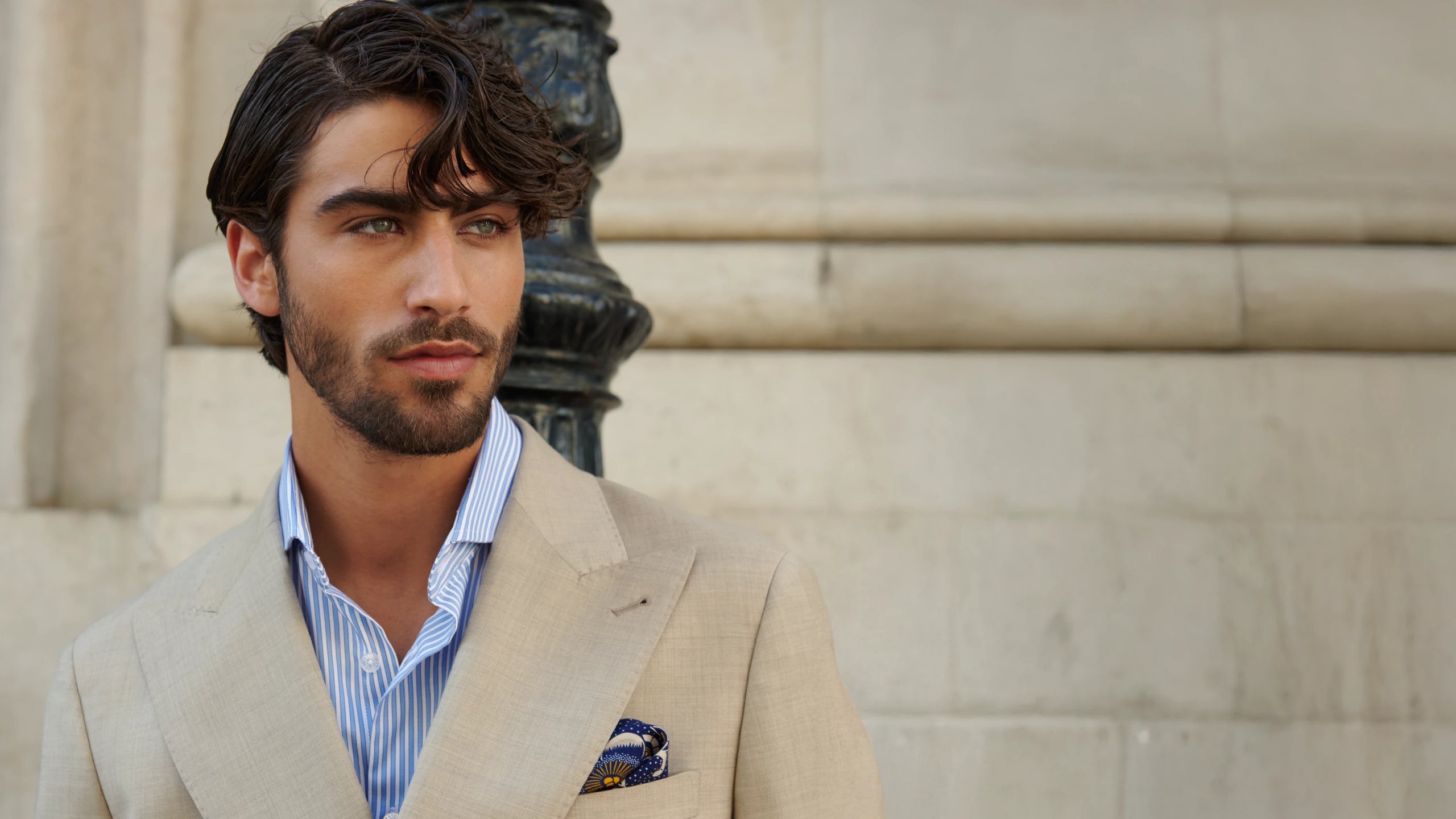 Man in a beige suit standing against a stone wall