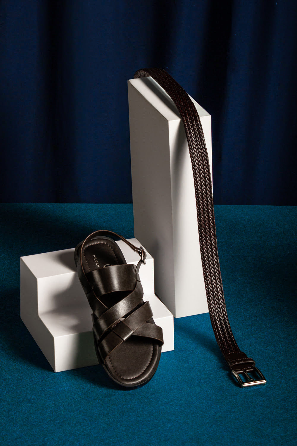 Black sandal with a strap on a white block against a blue background