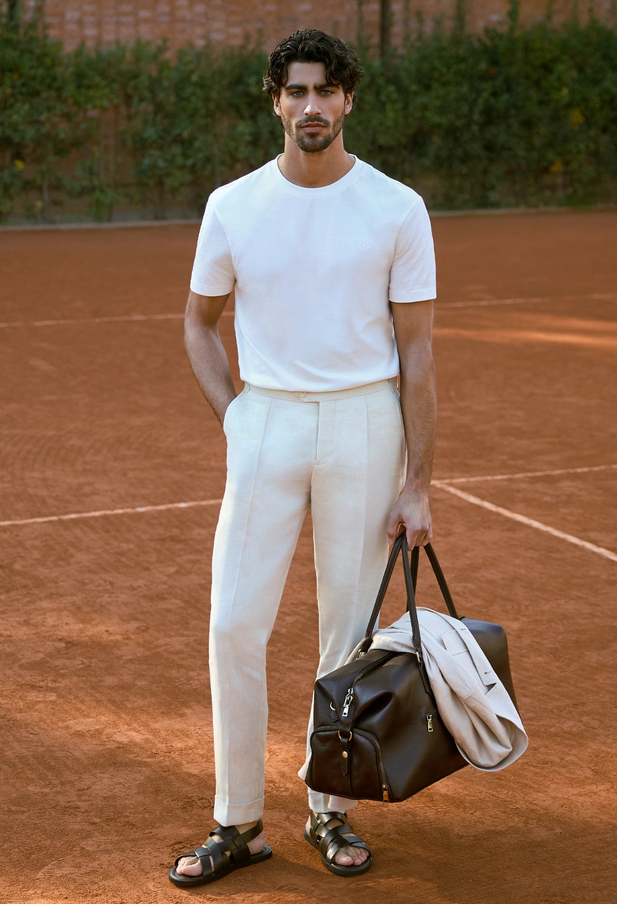 Man in white outfit holding bags on a tennis court