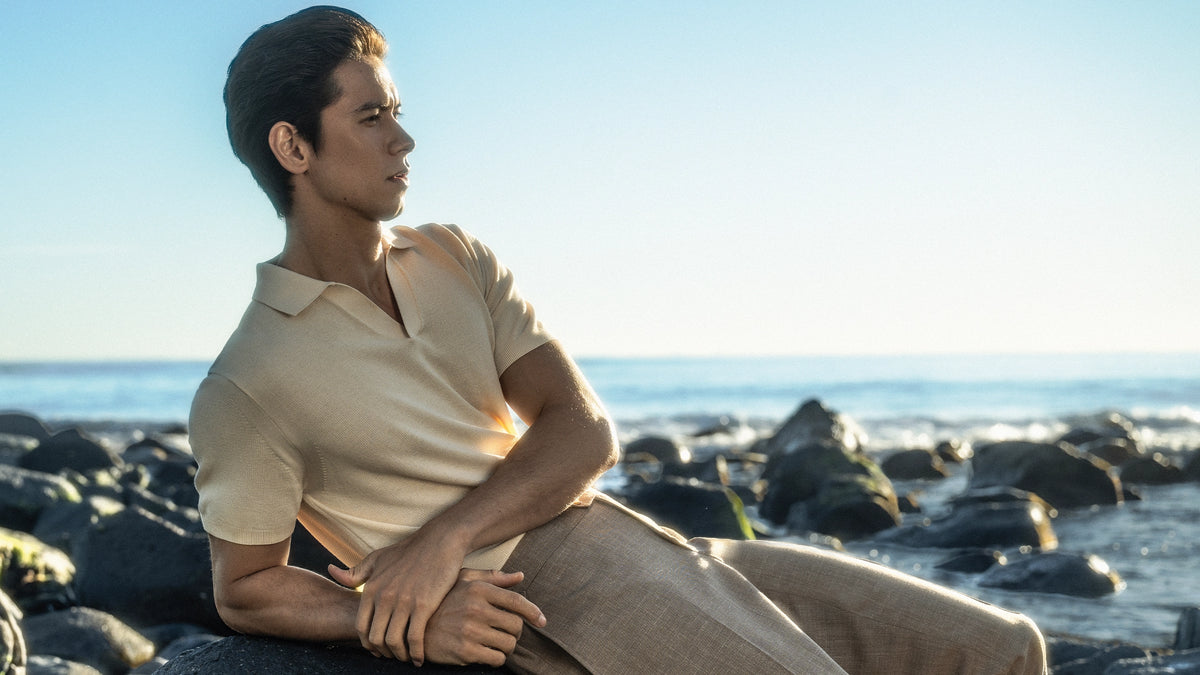 Man sitting on rocks by the ocean with a clear blue sky.