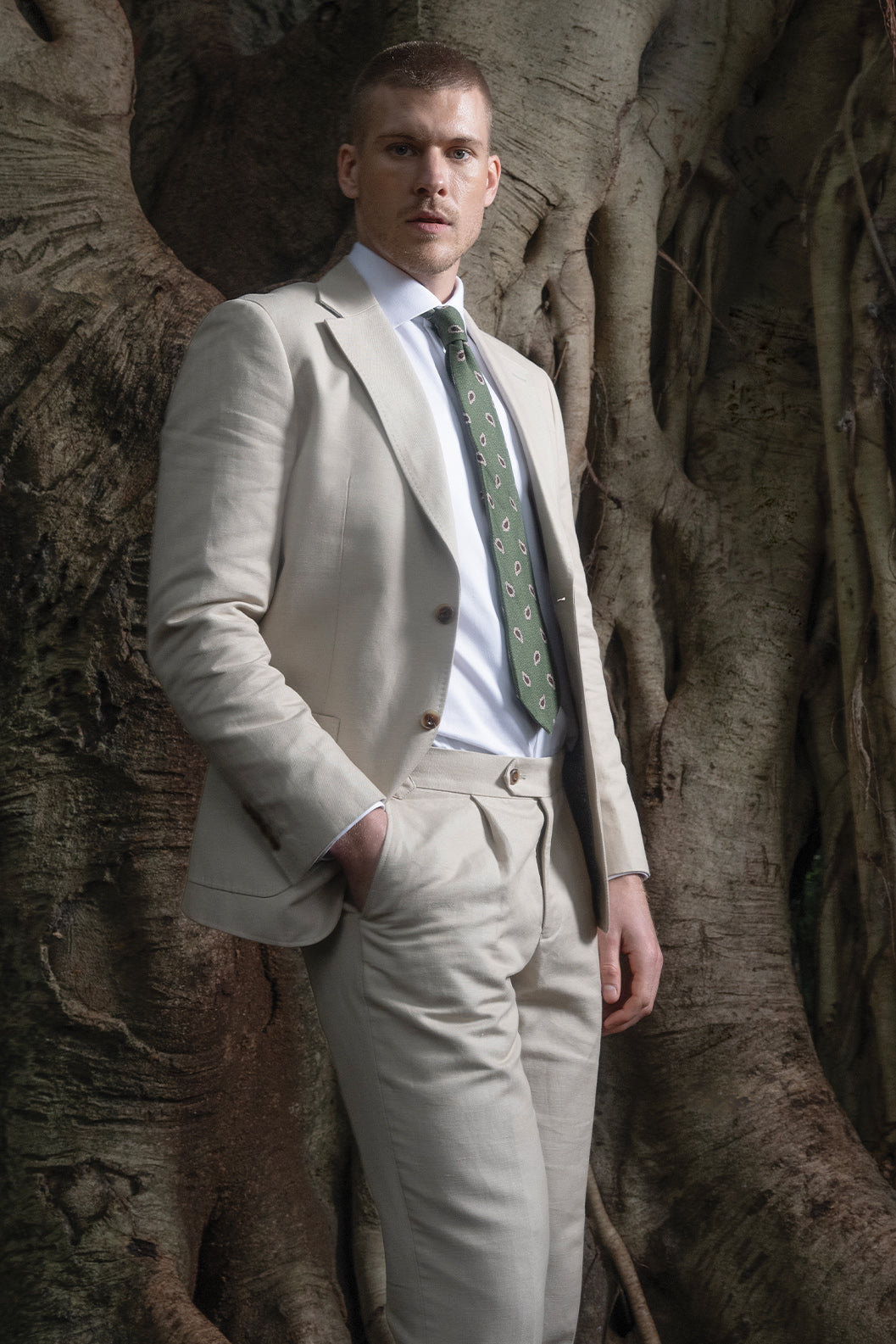 Man in a beige suit standing against a tree
