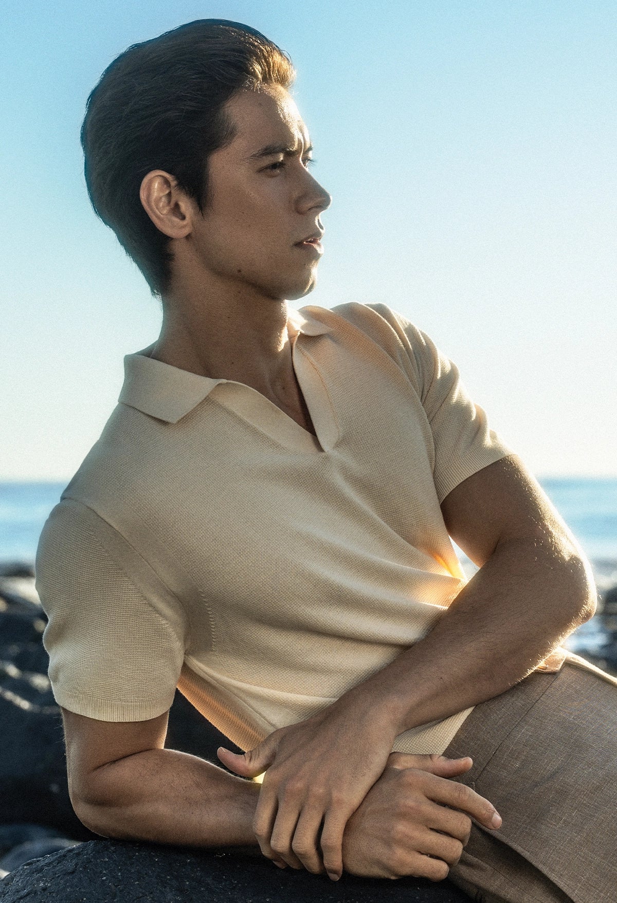 Man sitting by the ocean wearing a light-colored polo shirt.