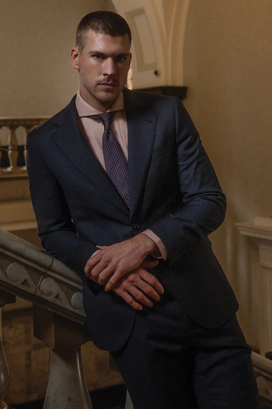 Man wearing blue suit with tie leaning against railing