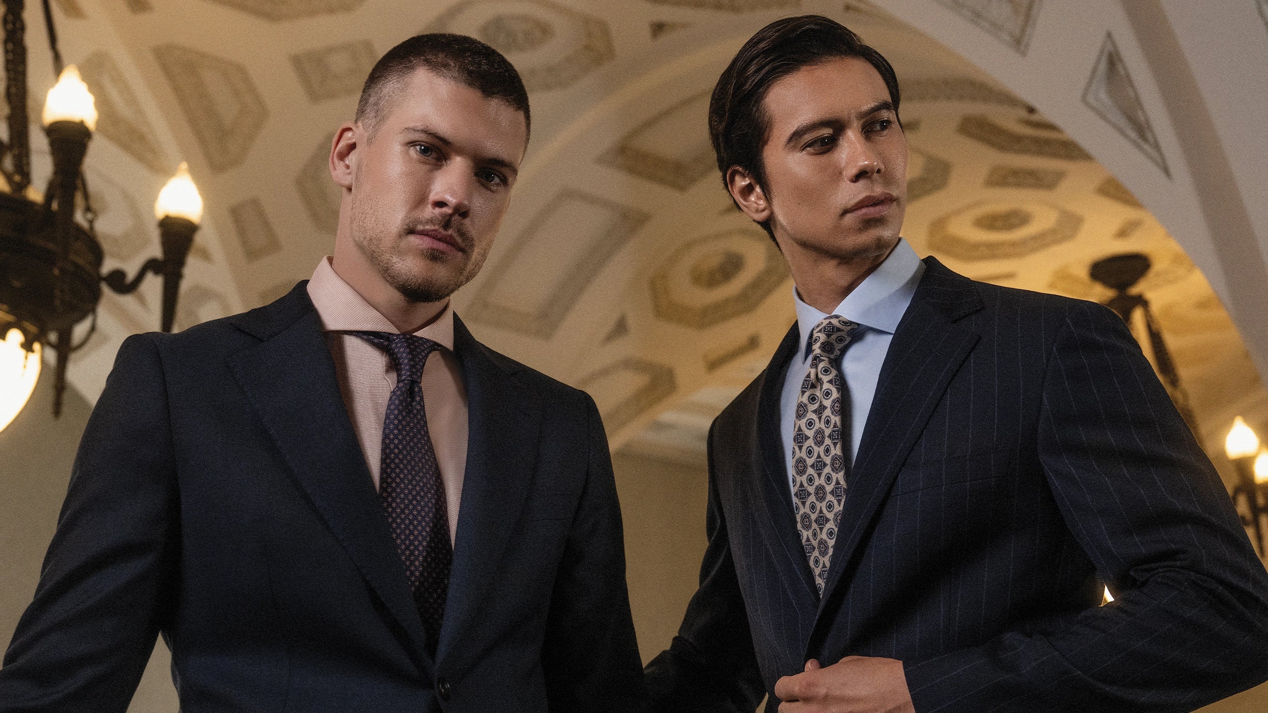Man wearing blue suit standing next to another man wearing a blue shirt